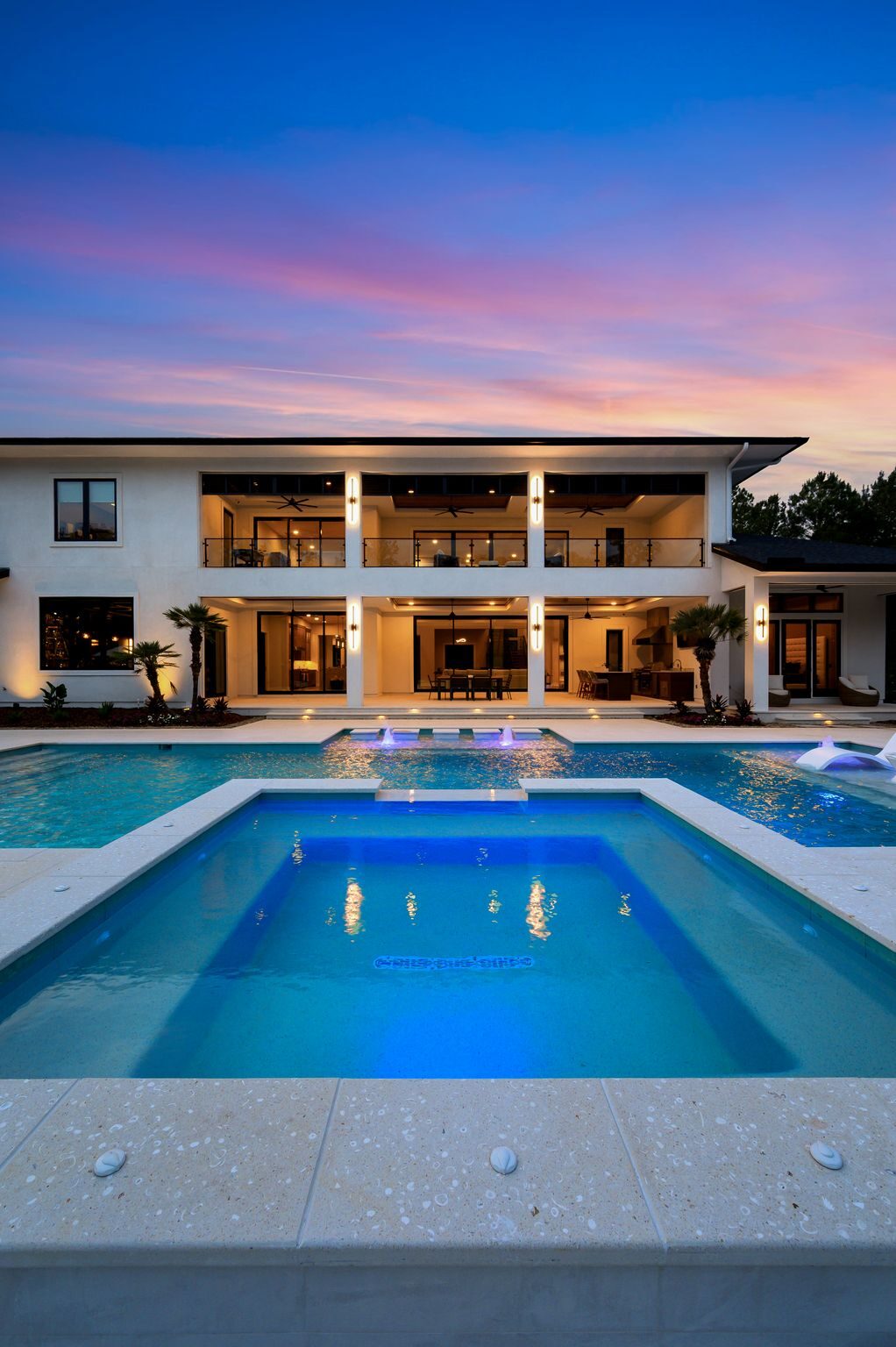 Symmetrical custom pool and raised spa glowing blue at twilight